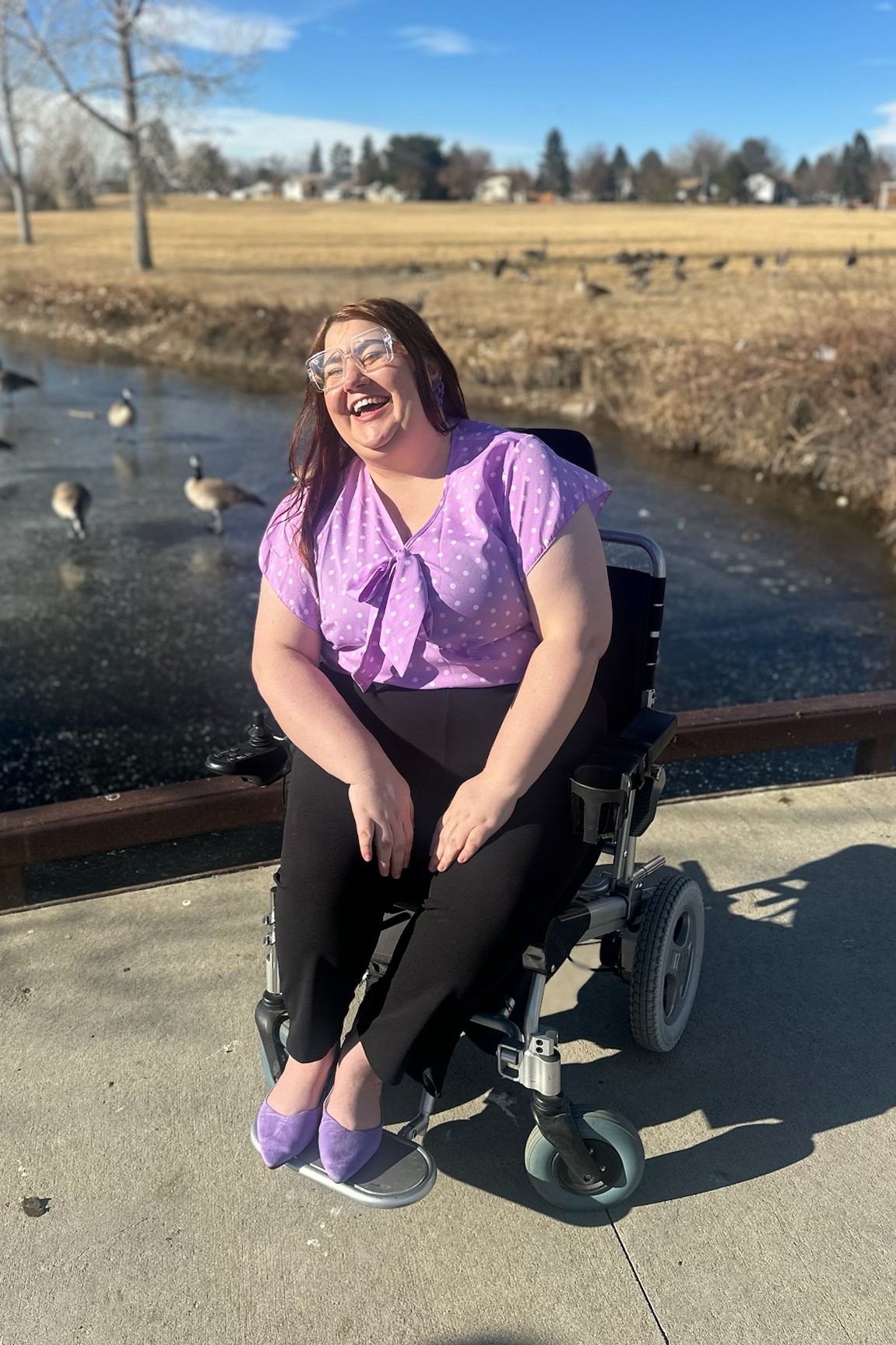 A woman is laughing while she sits in her wheelchair in a park.